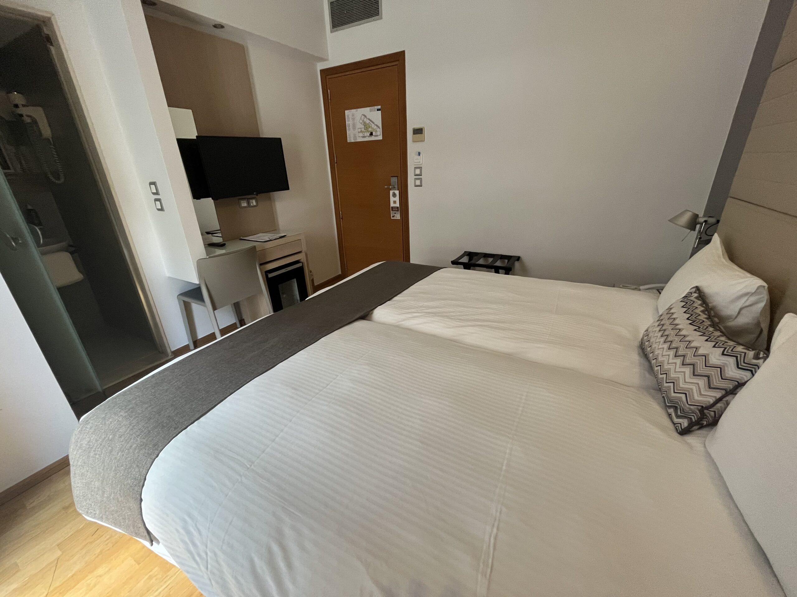 Интериор на стая с легло, телевизор, бюро и минихладилник в хотел Domotel Olympia, Солун.