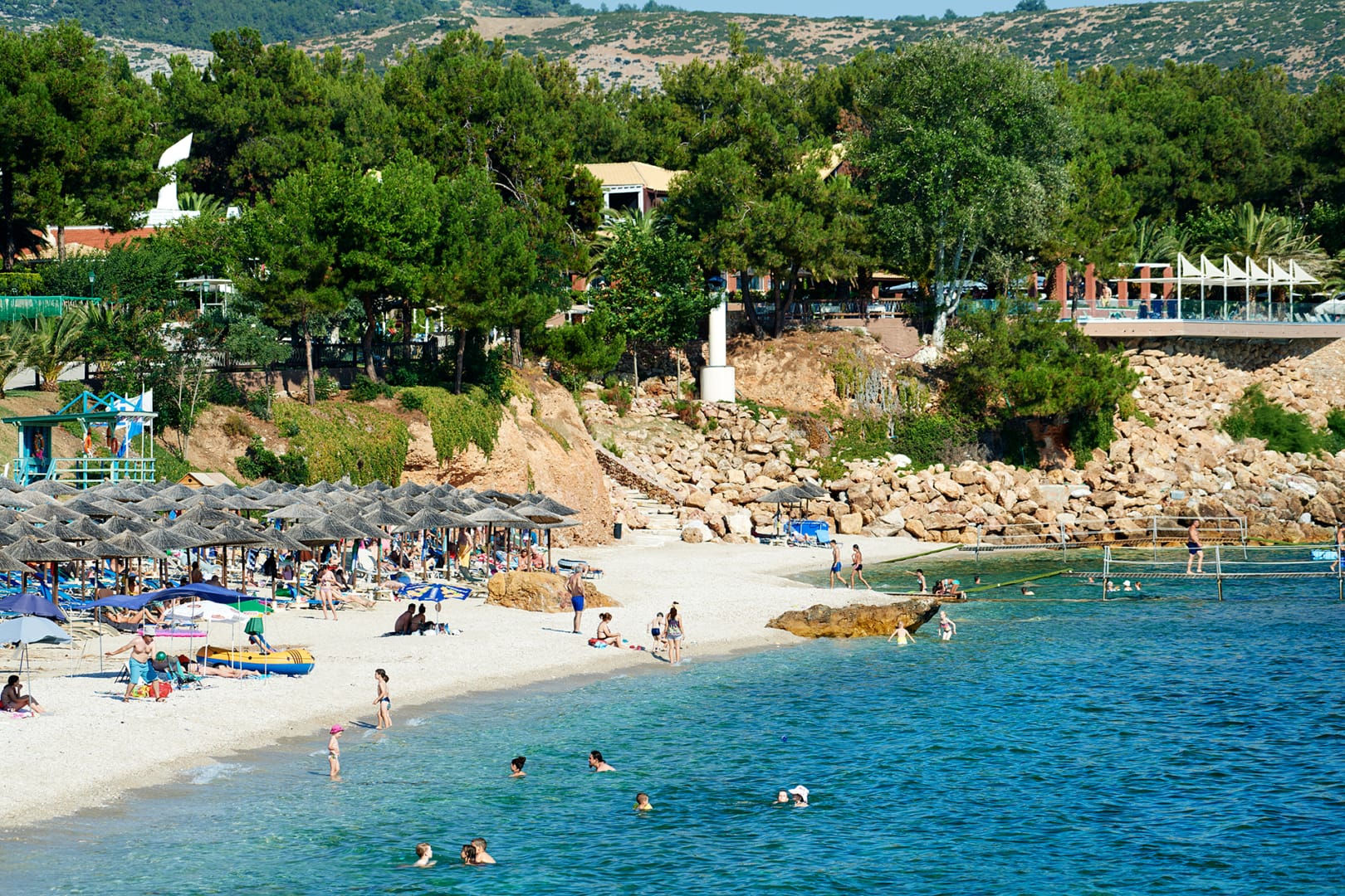 Плажът на Alexandra Beach Thassos Spa Resort 4* на остров Тасос, с кристално чисто море, чадъри и зеленина около хотела.