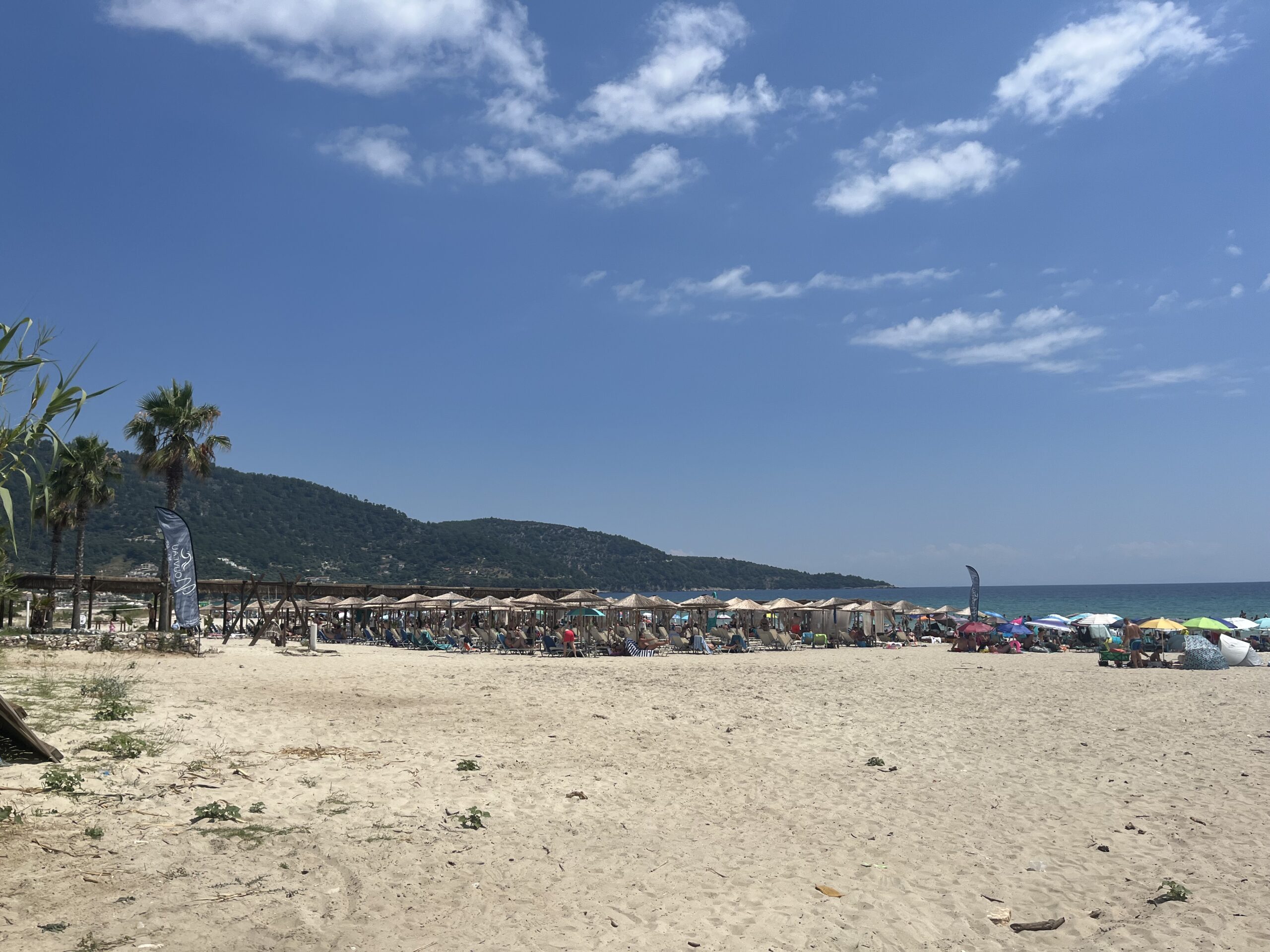 Широката пясъчна ивица на Golden Beach на остров Тасос, с плажни чадъри, шезлонги и зелени хълмове.