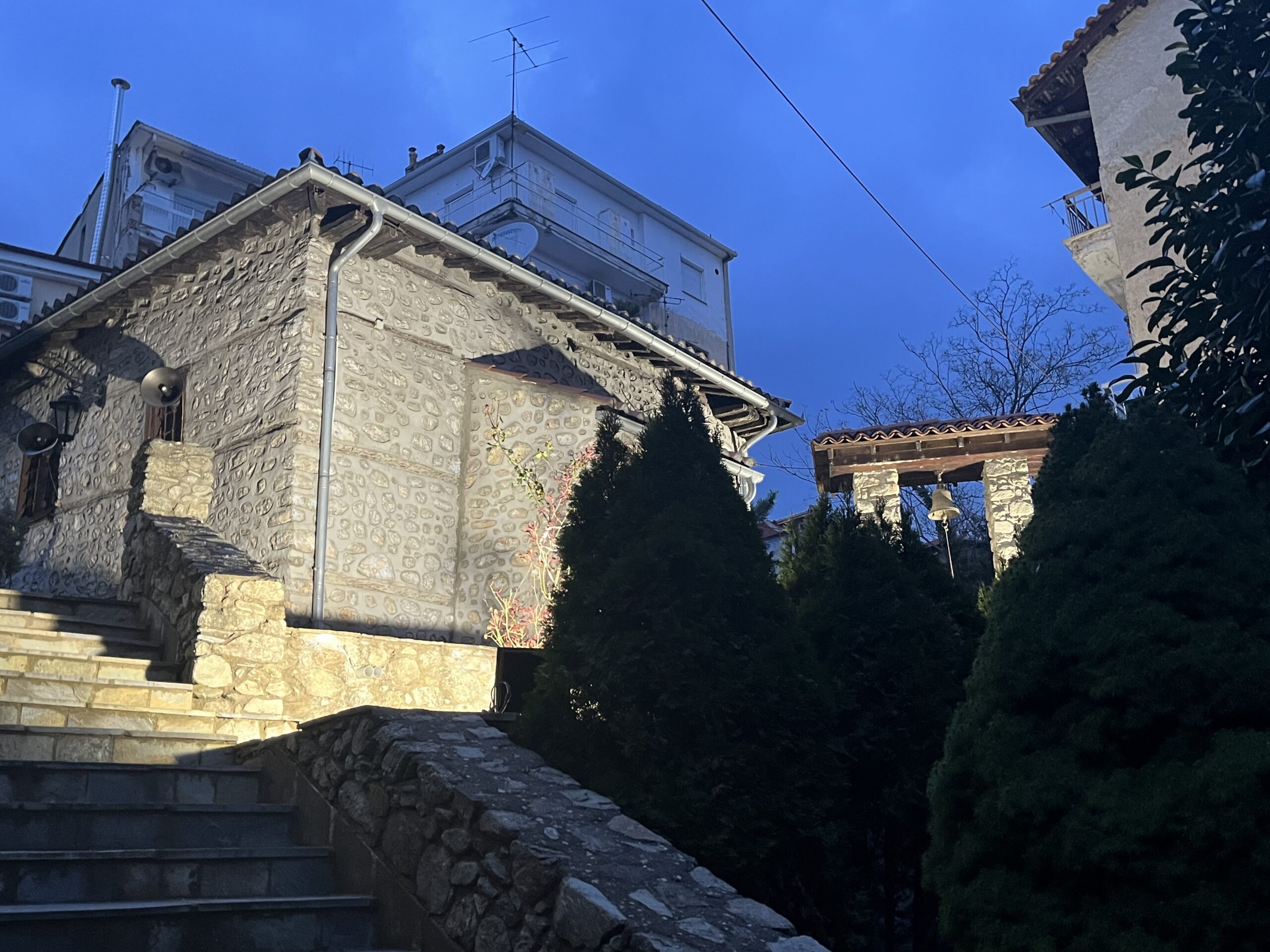 Каменна църква с осветена фасада, стълби и камбанария в Кастория привечер